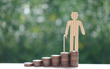 階段状に並べたコインの上に、杖を持った初老男性の木の板のシルエット